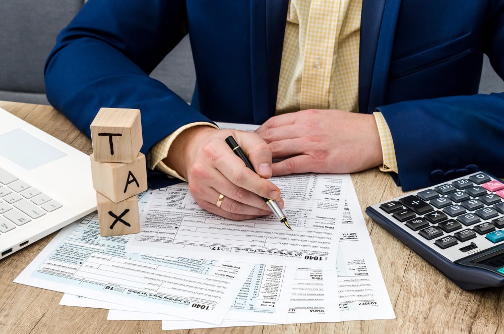 Accountant reviewing tax forms with calculator, laptop, and wooden tax blocks on desk, representing 
