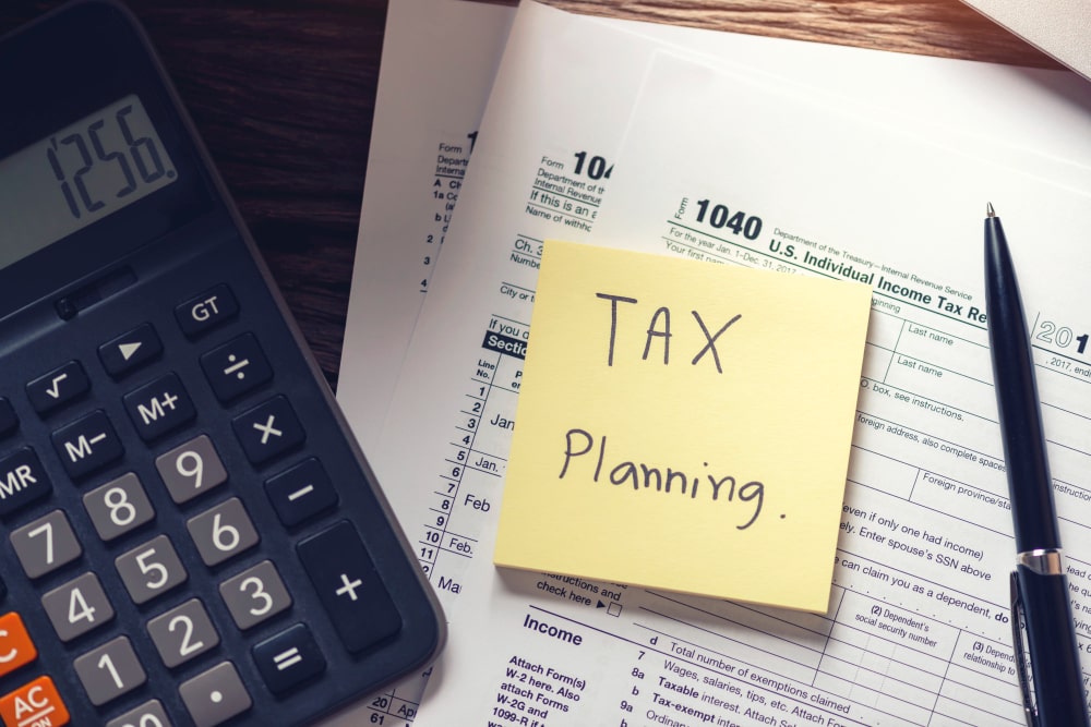 A calculator, a pen, and a yellow sticky note that reads 